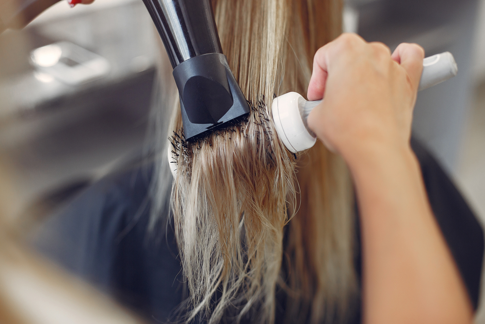 A woman helps blow dry her client's hair extensions, using good techniques.